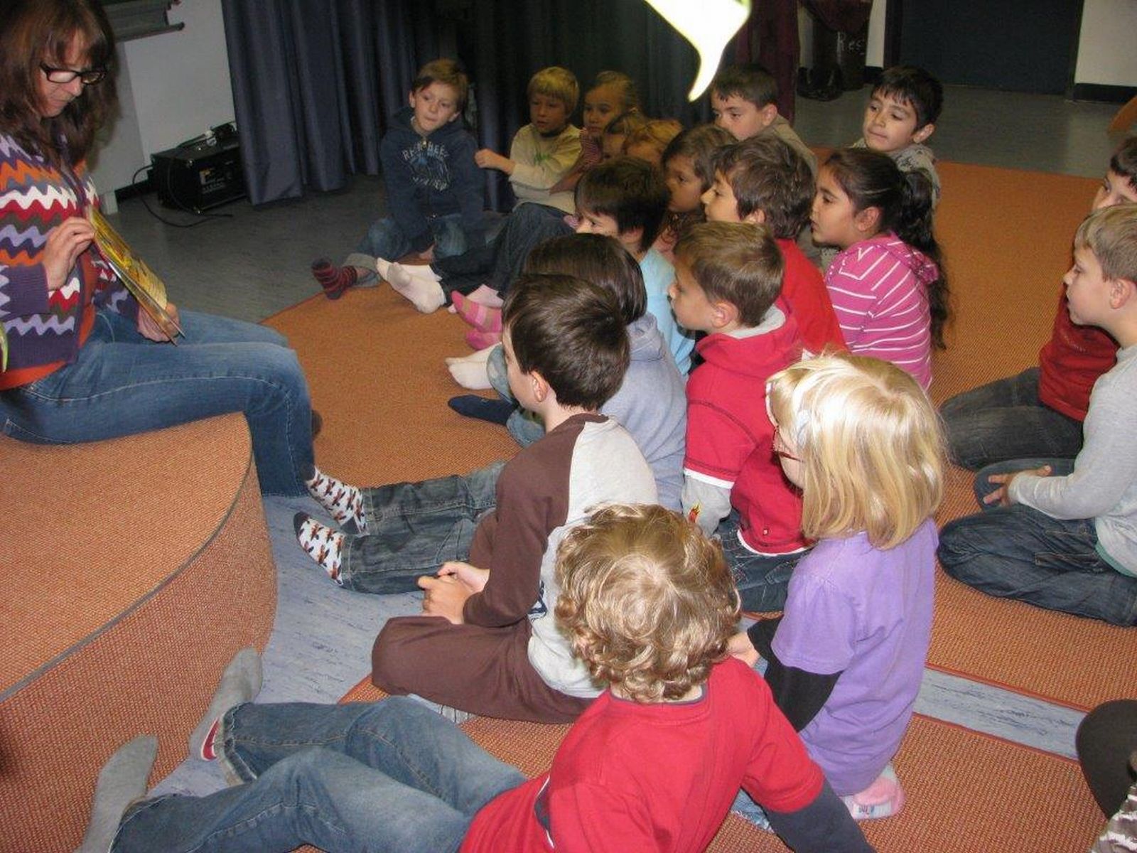  Kinder hören gespannt der Vorleserin zu 
