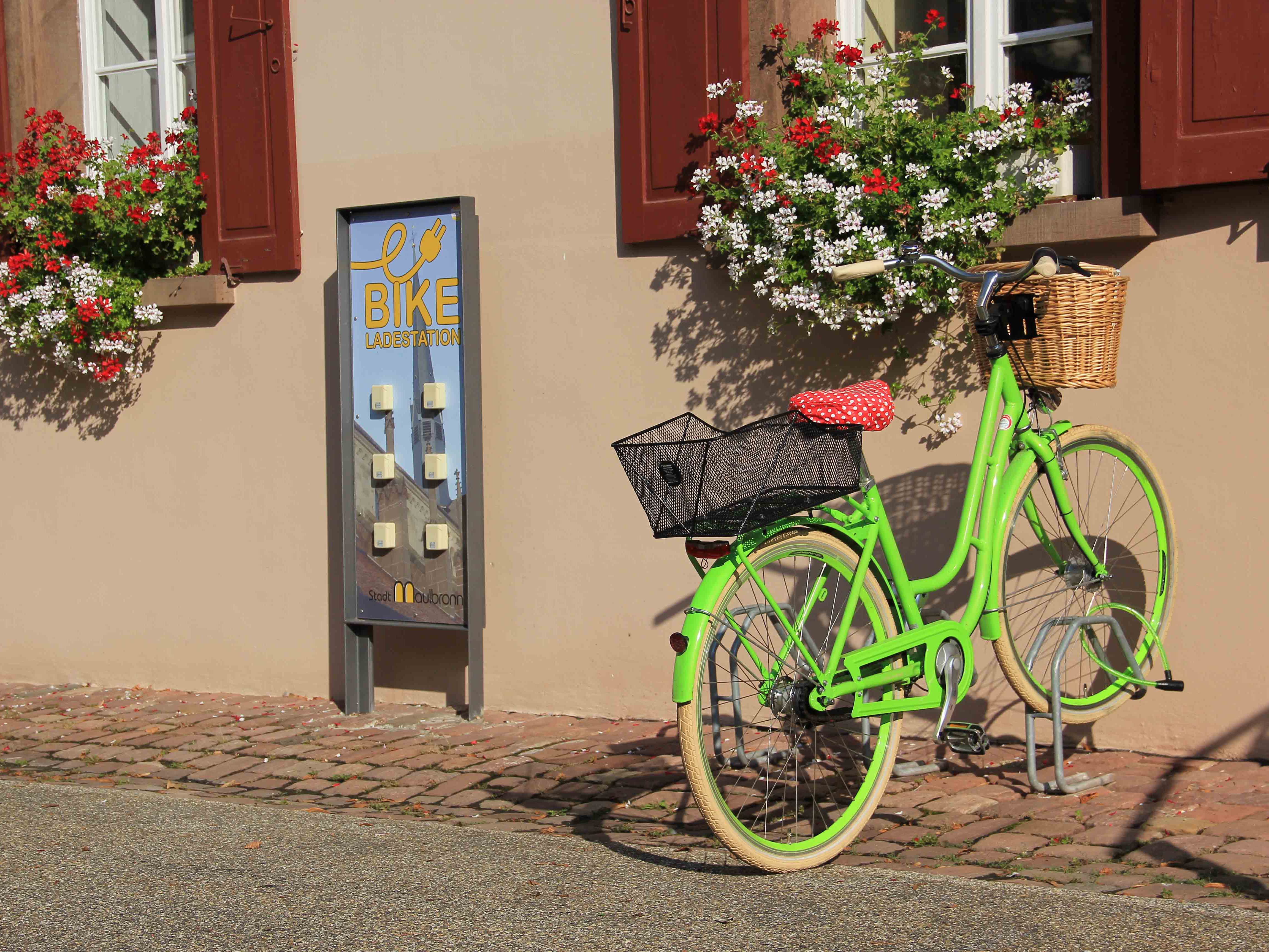 Giftgrünes Citybike vor dem Rathausgebäude, daneben eine E-Bike-Ladestation