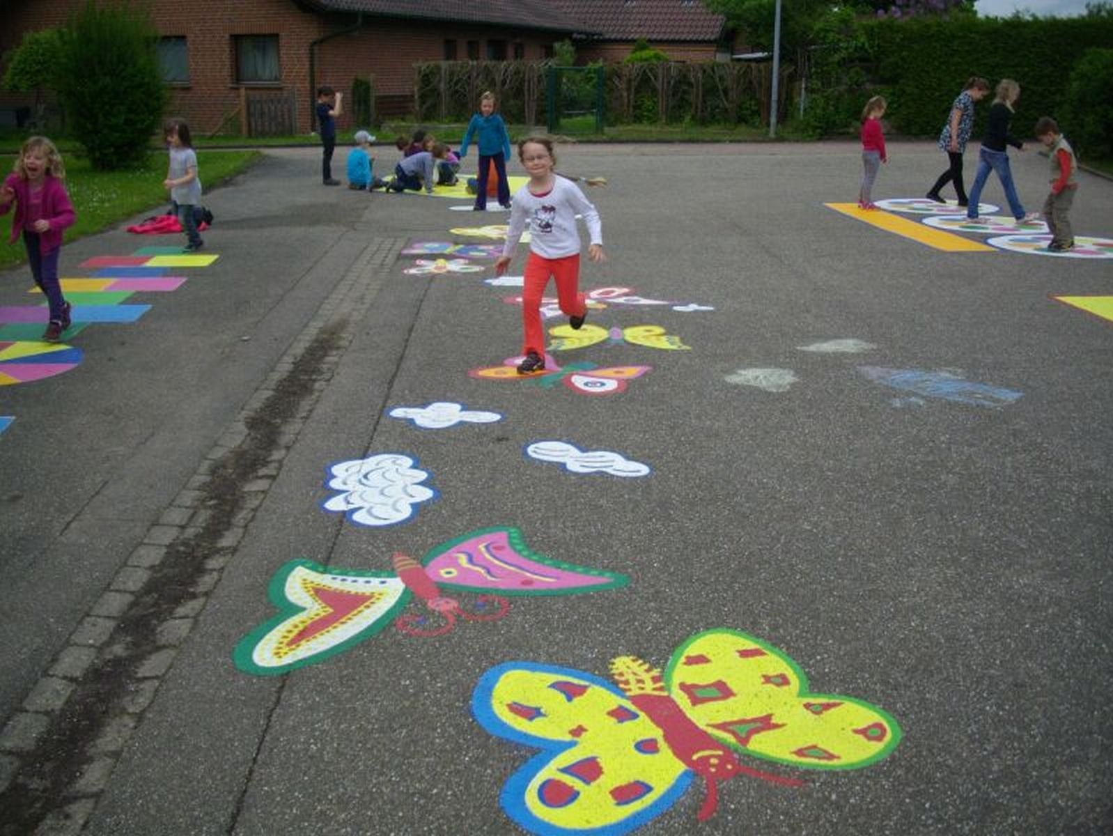 Kinder, die auf einem Schulhof spielen, auf dem Boden sind bunte Schmetterlinge mit Kreide aufgemalt