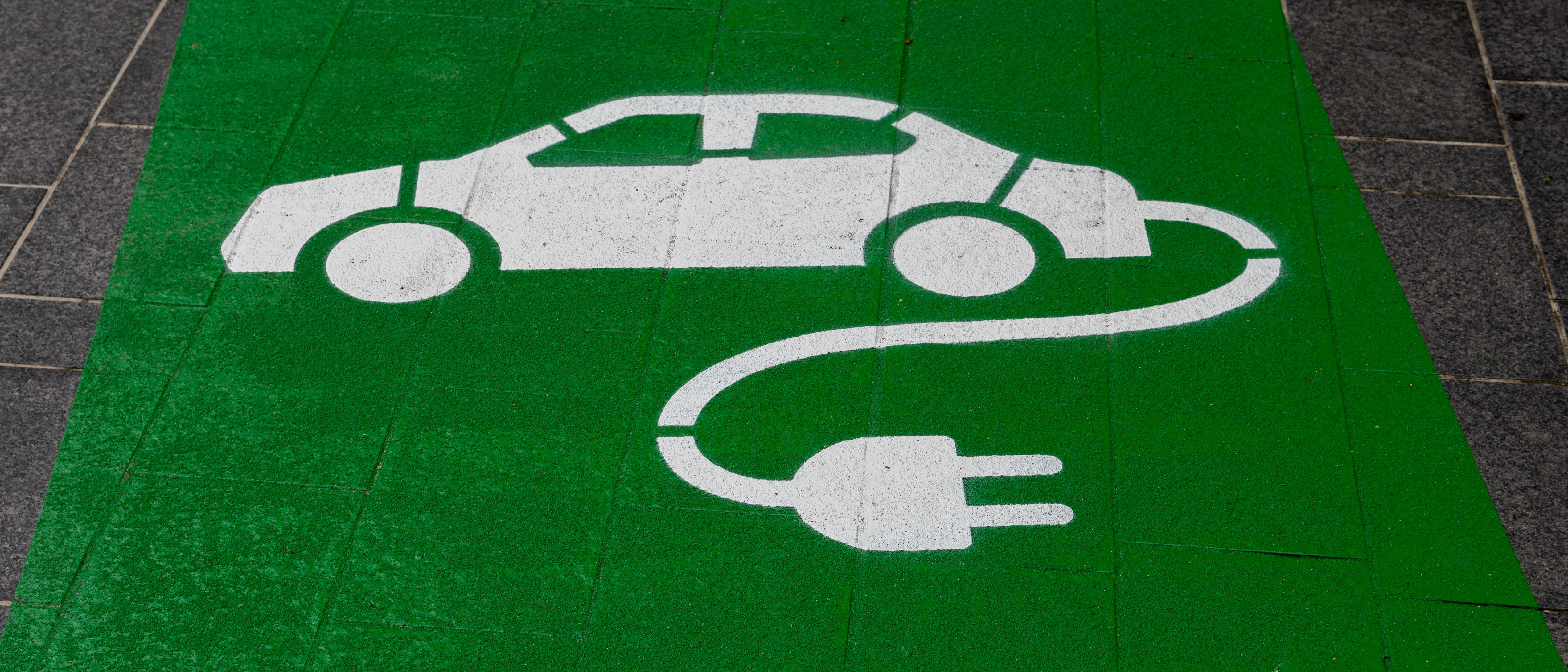 Zeichnung eines weißen Autos mit Kabel und Stecker auf grüner Fläche