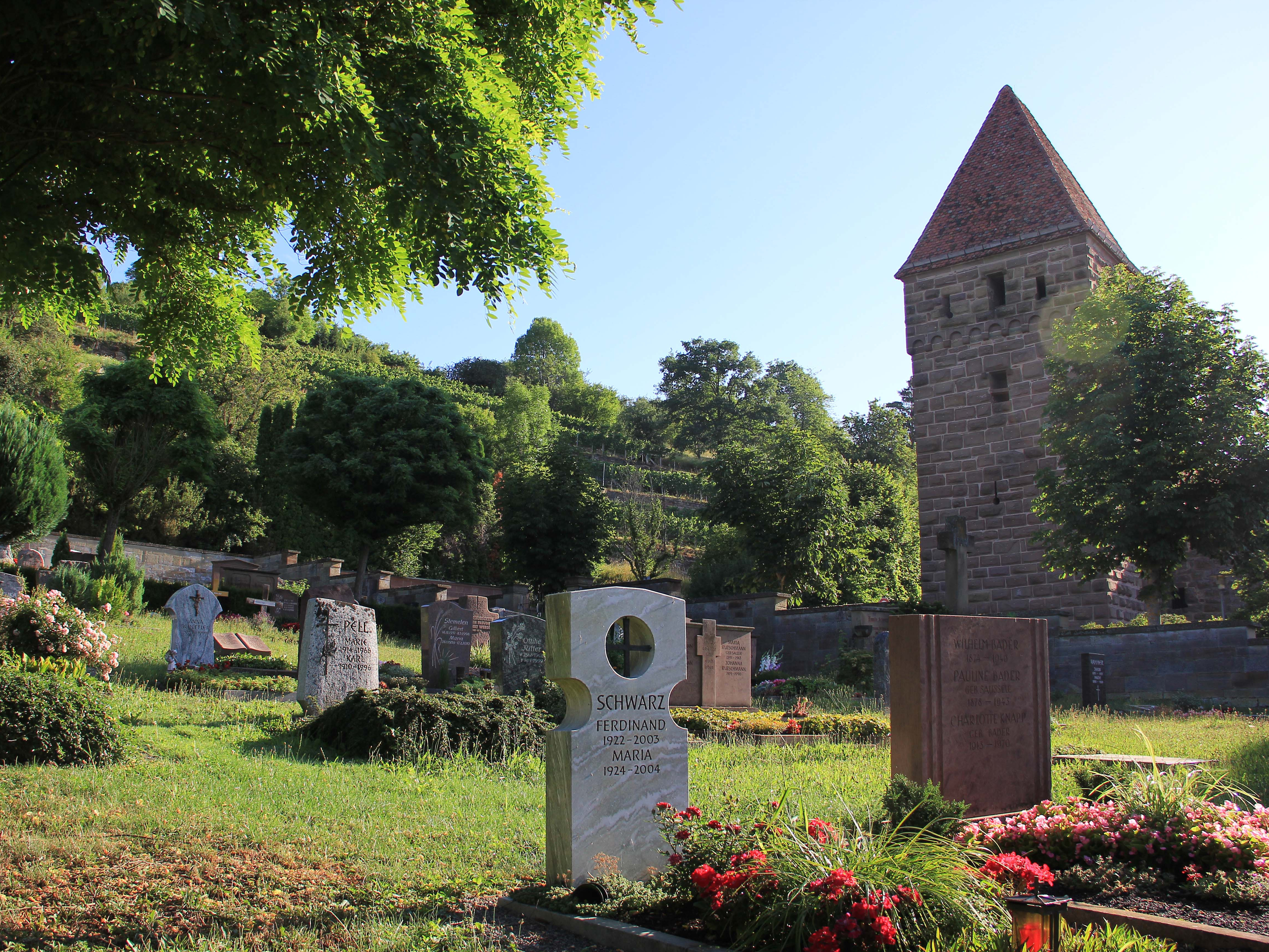 Blick auf Grabsteine, bepflanzte Gräber, im Hintergrund Bäume und ein mittelalterlicher Turm